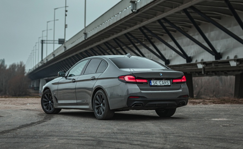 Tylny widok szarego BMW 5 Series na tle miejskiego krajobrazu. Elegancki sedan do wynajmu w SK CARS, idealny na każdą podróż.