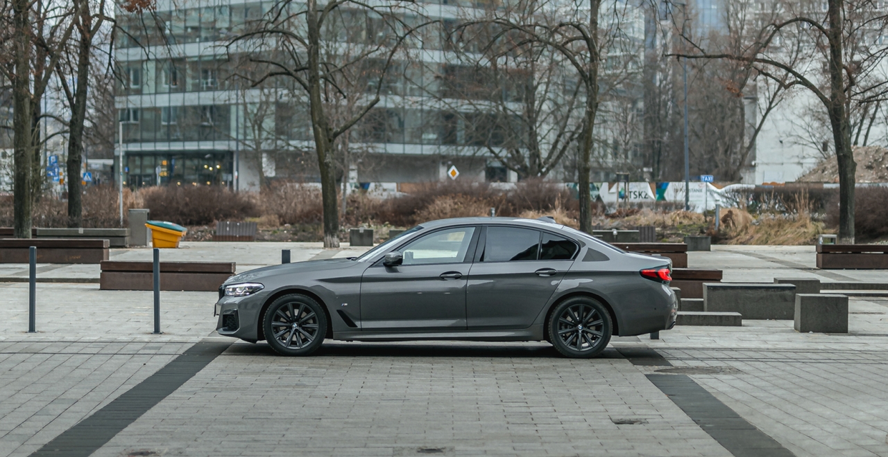 slide 2 - Stylowy sedan BMW 5 Series na tle miejskiej architektury. Wynajem samochodów premium w SK CARS.